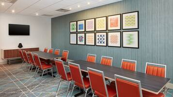 A conference room with a long table, orange chairs, a flat-screen TV, and patterned artwork on the wall.