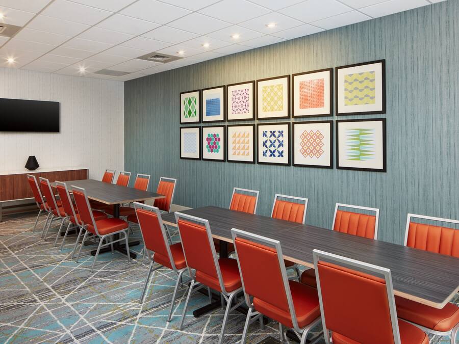 A conference room with a long table, orange chairs, a flat-screen TV, and patterned artwork on the wall.