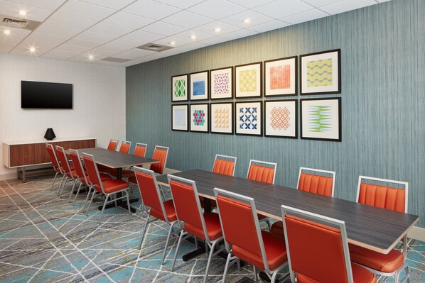 A conference room with a long table, orange chairs, a flat-screen TV, and patterned artwork on the wall.