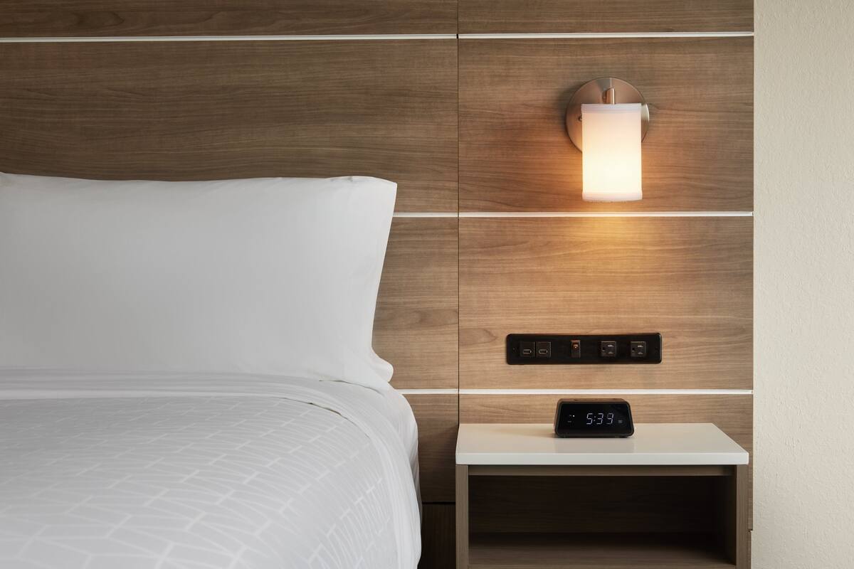 Un lit bien fait, avec une couette blanche et une tête de lit dotée d’un éclairage intégré.