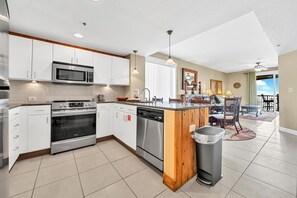 Enjoy cooking in this well-equipped kitchen with a central island, sink, and appliances, adjacent to a dining area and balcony with a view.