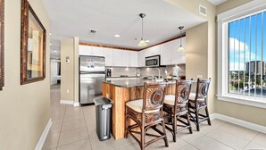 A modern kitchen with a central island, white cabinets, stainless steel appliances, and a large window with a city view. - 🌞Beach Front-Corner Unit-Grand Panama 1-409🌞 (Panama City Beach)