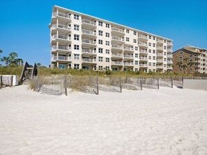 Un hôtel à plusieurs étages, doté de balcons, situé près d’une plage de sable.
