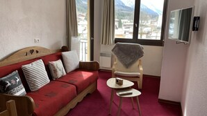A cozy room with a red sofa, a small table, a chair, and a TV on the wall. - Cosy 2-room apartment in the heart of Chamonix, Mont Blanc view (Chamonix-Mont-Blanc)