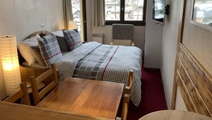 A hotel room with a bed, a wooden table, a chair, a lamp, and a TV mounted on the wall. - Cosy 2-room apartment in the heart of Chamonix, Mont Blanc view (Chamonix-Mont-Blanc)