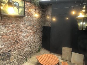 A brick wall with a wooden table and chairs, string lights, and a lantern.