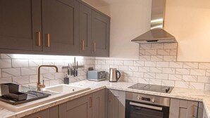 A modern kitchen with grey cabinets, a stainless steel range hood, a built-in oven, and a marble backsplash.