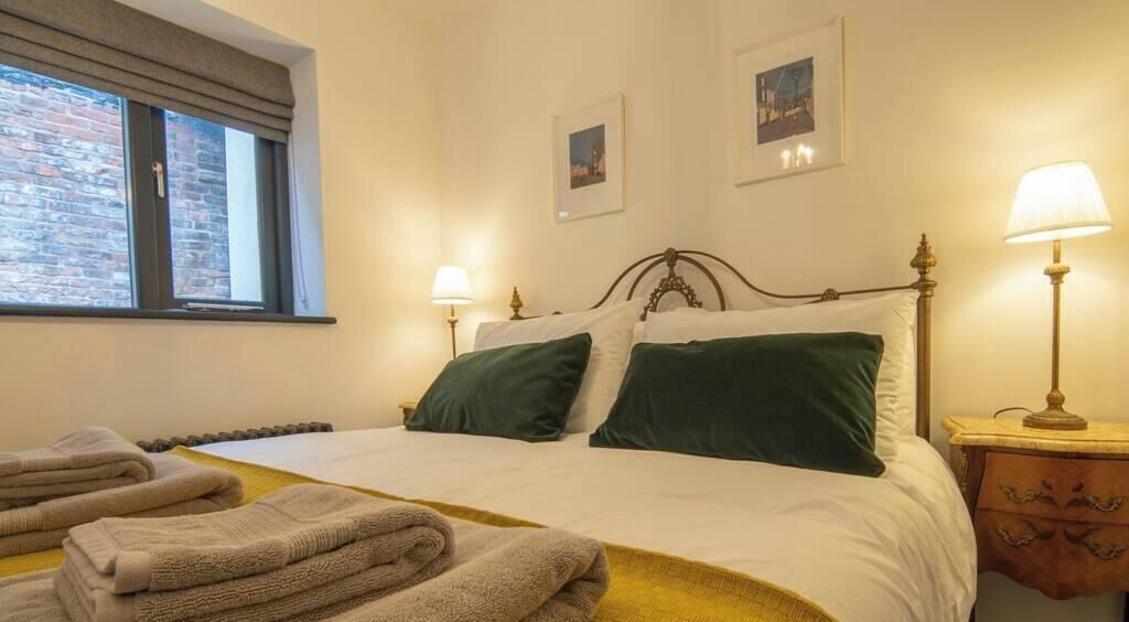 A hotel room with a bed, two bedside lamps, a window with a view, and a wall with two framed pictures.
