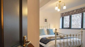 A bedroom with a bed, a window with a view of a stone wall, and a chandelier. - Heart of Macclesfield Former 16th Century Inn (Macclesfield)