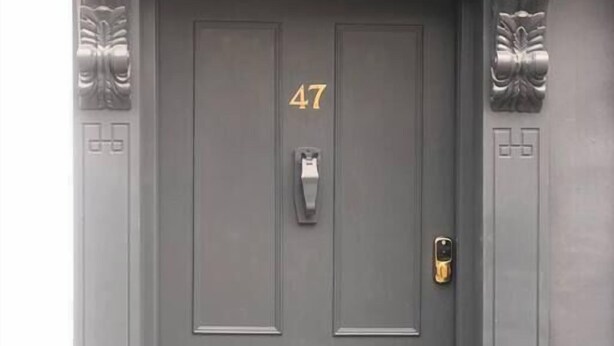 Une porte gris foncé portant le numéro 47, une fente pour le courrier, un interphone et un trou de serrure.