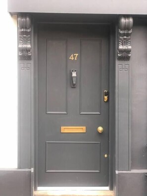 Une porte gris foncé portant le numéro 47, une fente pour le courrier, un interphone et un trou de serrure.