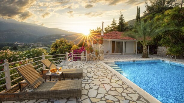 Ein Poolbereich mit Blick auf Berge, eine Steinterrasse und eine Lounge mit Korbmöbeln.