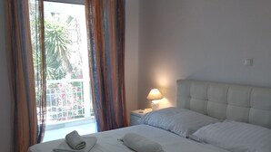 Ein ordentlich bezogenes Bett mit Handtüchern, einer Nachttischlampe und Blick auf einen Balkon mit Vorhängen.