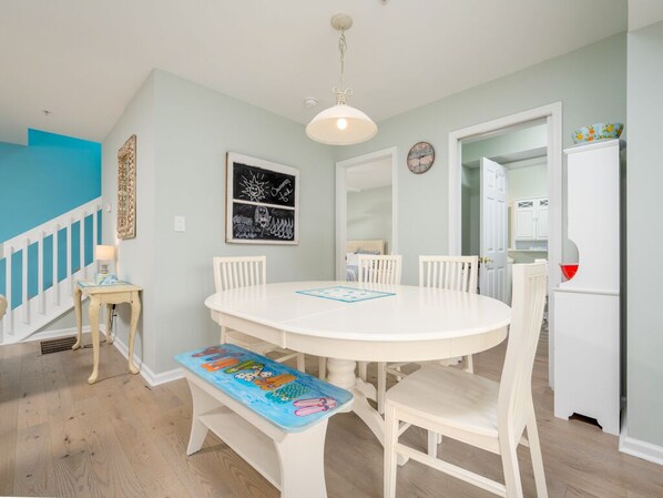 A dining area with a round table, white chairs, and a bench with a children's book.