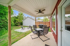 Une terrasse extérieure avec une table et des chaises, un ventilateur de plafond et une vue sur un jardin.