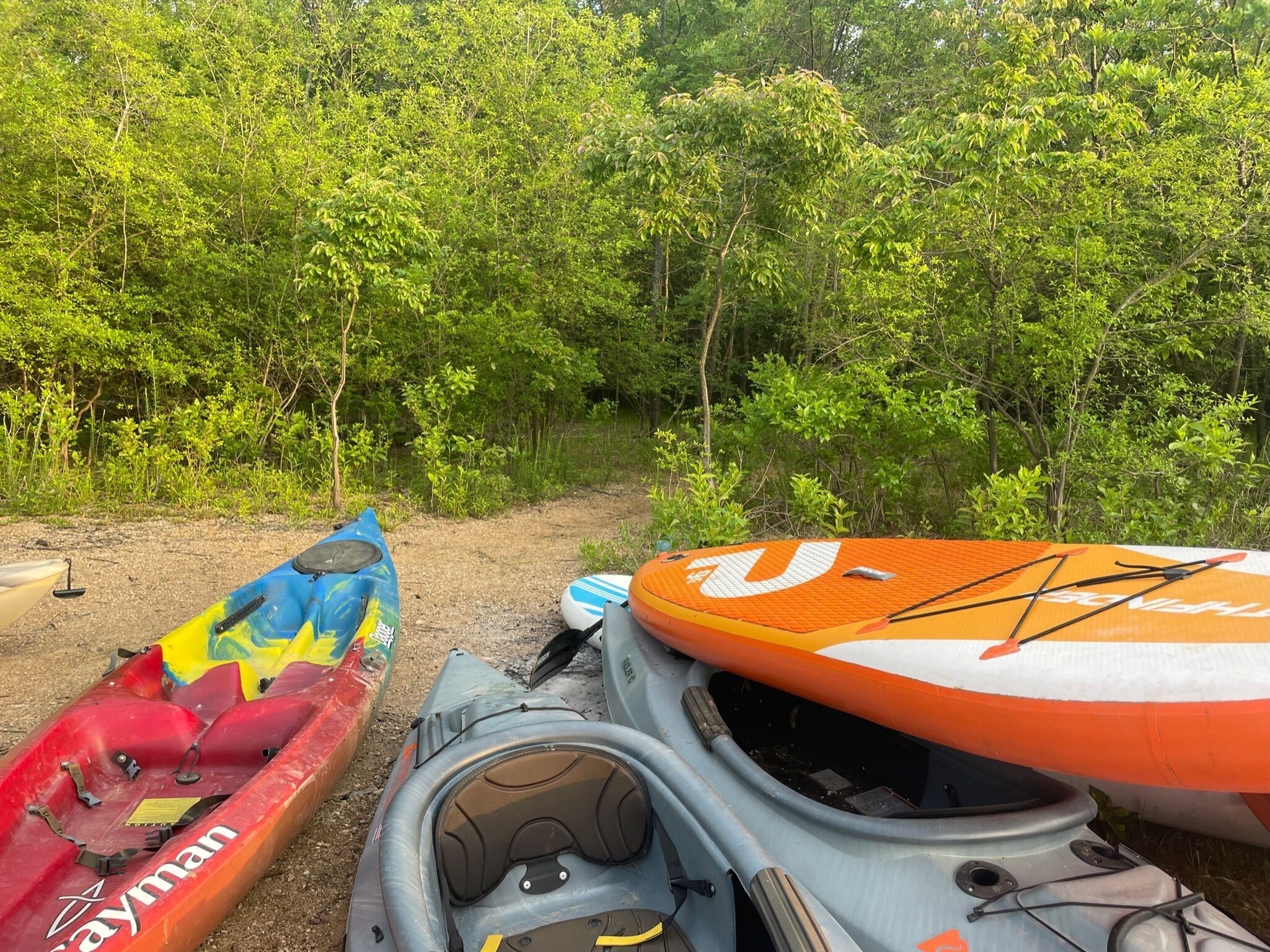 Kayaks and a paddleboard by a forest path.