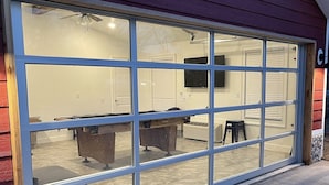 Une grande porte de garage transparente, permettant de voir l’intérieur du garage, qui comprend un établi et une chaise.