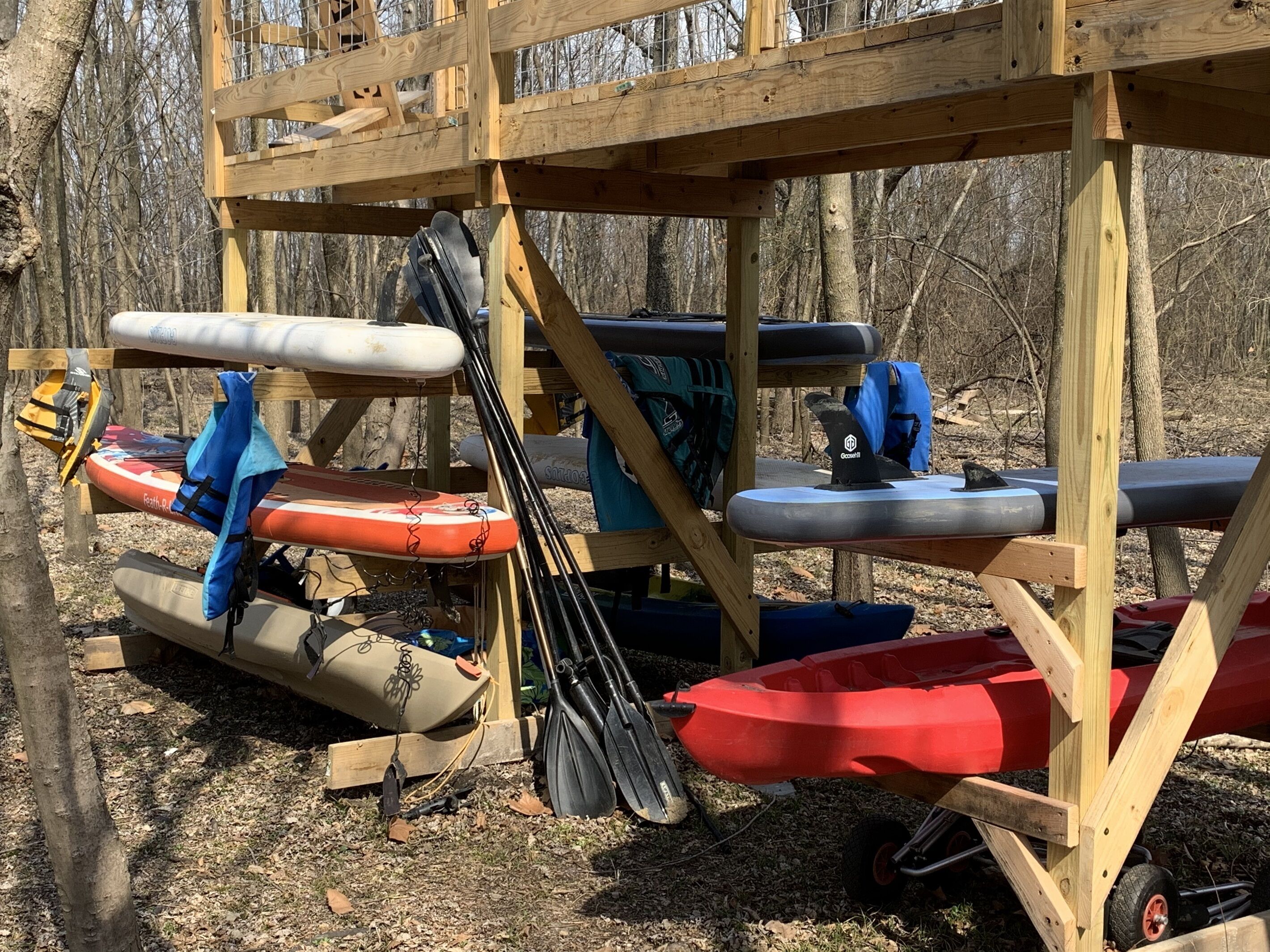 A wooden structure with kayaks and paddles stored underneath.