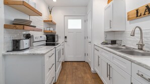 Une cuisine moderne avec des armoires blanches, des étagères en bois, un grille-pain, un four et un évier.