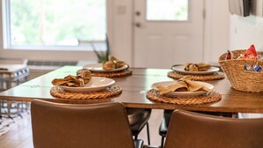 Une table à manger dressée avec des assiettes, des serviettes et un panier contenant divers condiments.
