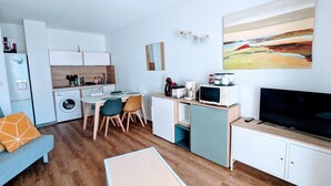 Ein kompakter Wohnbereich mit Küchenzeile, Essplatz, Sofa, Fernseher und einem Bild an der Wand.