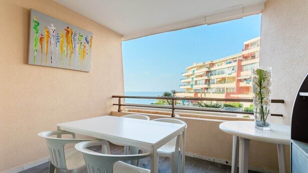 Ein Balkon mit weißem Tisch und Stühlen, einem Bild an der Wand und Blick auf ein Gebäude über dem Wasser.