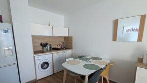 Eine kleine Küche mit Waschmaschine, einem Esstisch mit Stühlen und einem kleinen Kühlschrank.