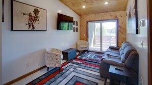 Una sala de estar moderna con un sofá, sillas, un televisor y un ventanal grande.