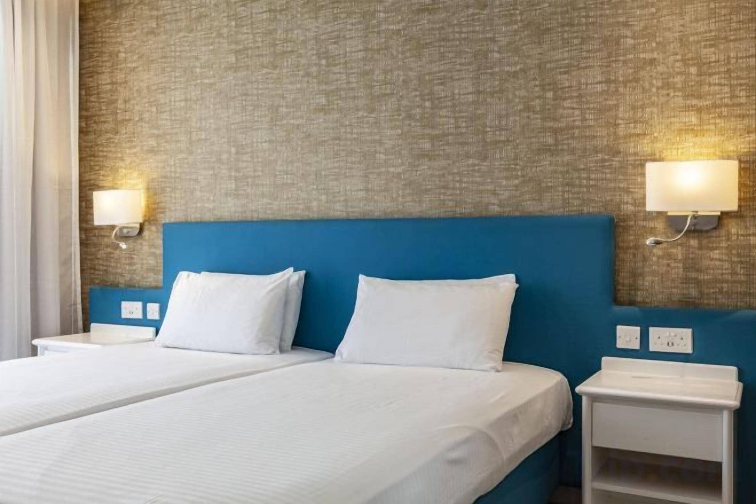 Hotellihuone, jossa on suuri sänky, kaksi yöpöytää ja kuvioitu seinä.