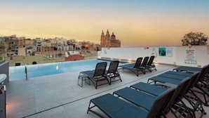 A rooftop pool area with lounge chairs and a view of a historic building. - Pergola Hotel & Spa (Mellieha)