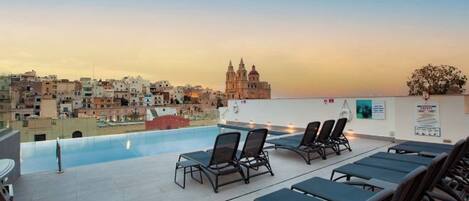 A rooftop pool area with lounge chairs and a view of a historic building.