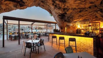 An outdoor dining area with a bar, tables, and chairs, set against a rocky backdrop.