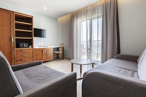 Uma sala de estar moderna com sofá, televisão na parede, um armário de madeira e varanda com cortinas.