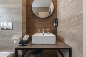 A modern bathroom with a rectangular sink, a round mirror, and a towel dispenser.