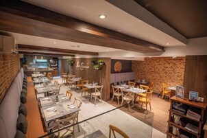 A restaurant with a modern interior, featuring wooden beams, brick walls, and a mix of wooden and upholstered seating.