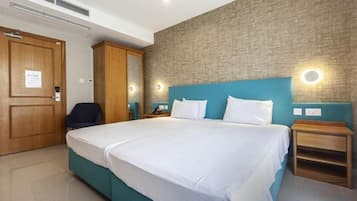 Quarto de hotel com uma cama grande, um guarda-roupa de madeira, uma escrivaninha com cadeira e um candeeiro fixado na parede.