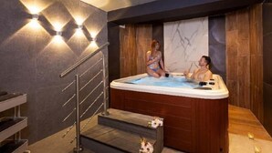 A modern bathroom with a wooden bathtub, a glass shower enclosure, and a marble wall. - Pergola Hotel & Spa (Mellieha)