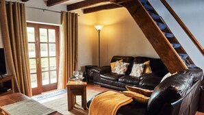 A cozy living room with a leather sofa, a wooden coffee table, and a floor lamp. - Stone Cottage Retreat with Pool & Lakeside (St Clears)