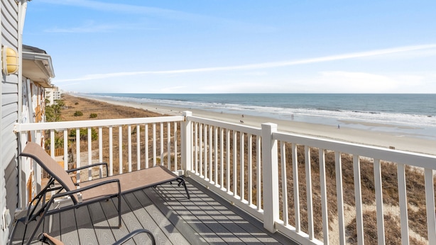 A wooden deck with a white railing overlooking a beach.