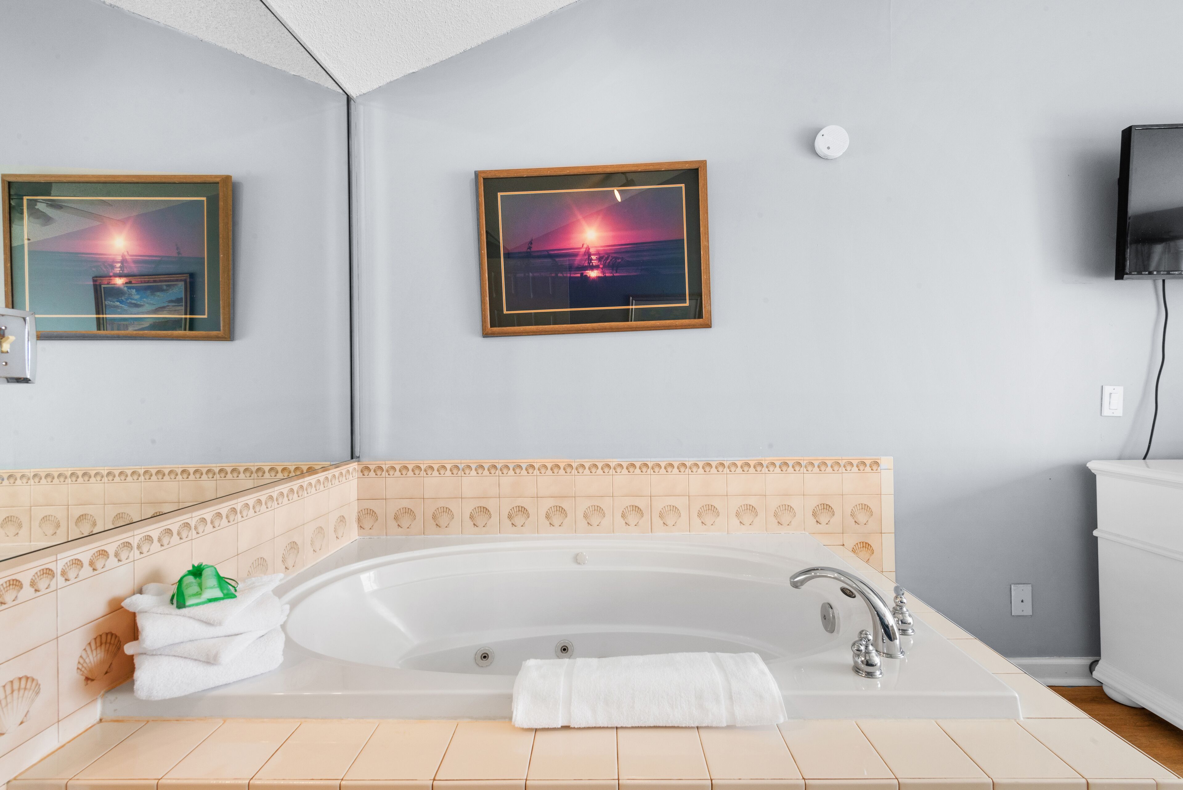 A bathroom with a large bathtub, framed pictures on the wall, and a tiled backsplash.