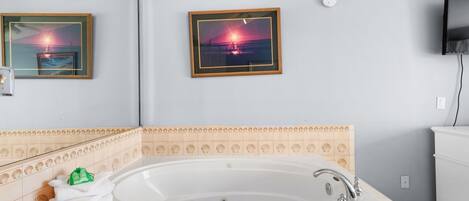 A bathroom with a large bathtub, framed pictures on the wall, and a tiled backsplash.