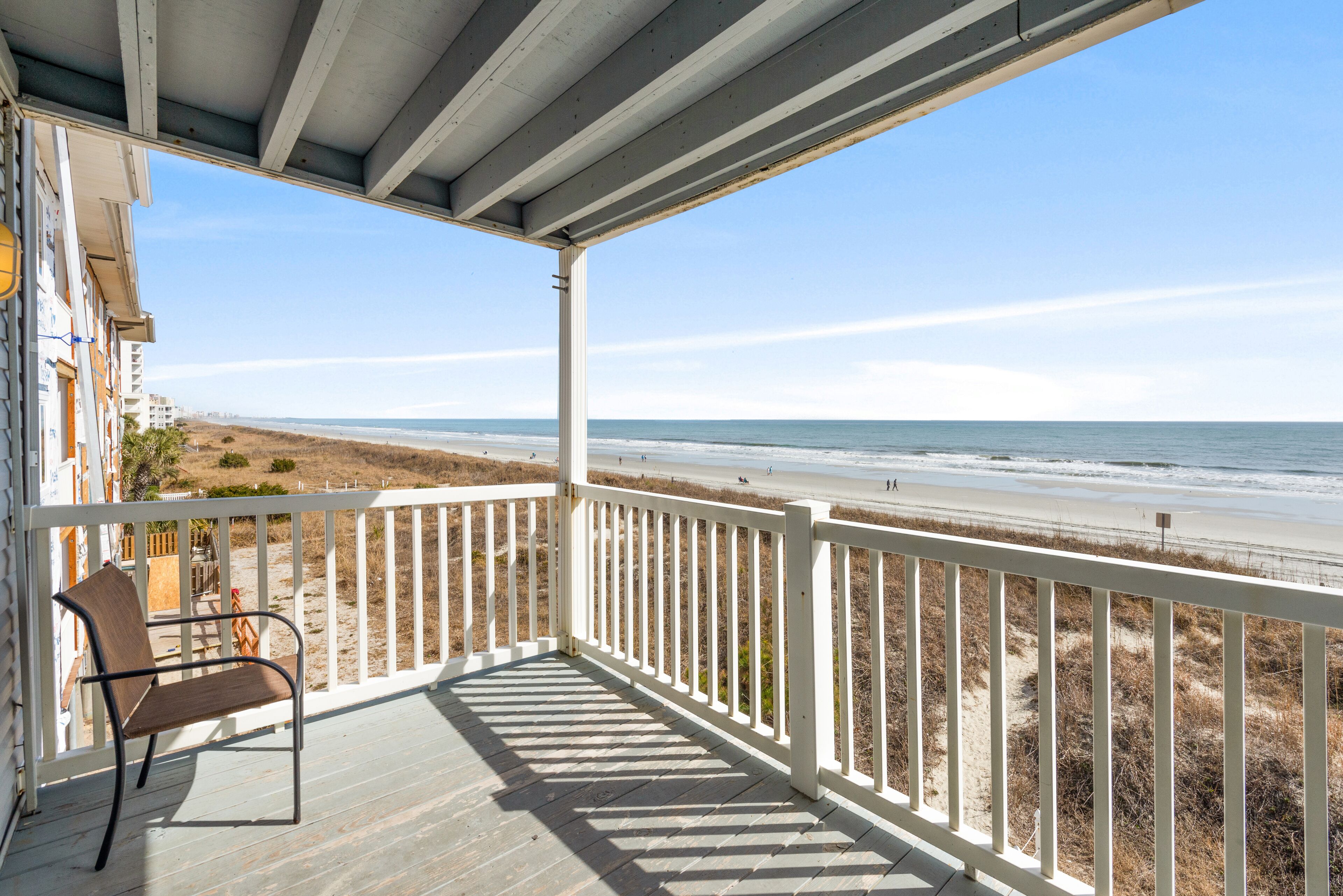 A wooden deck with a white railing overlooking a beach.