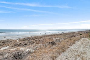 A beach with a sandy path, a fence, and a clear sky.
