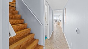 A staircase with wooden steps and white walls leading to a hallway with a tiled floor.