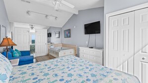 A bedroom with a bed, a ceiling fan, a TV, a dresser, and a bathroom visible through an open door.