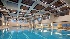 Une grande piscine intérieure dotée d’un design moderne au niveau du plafond, de grandes fenêtres et d’espaces aménagés pour s’asseoir.