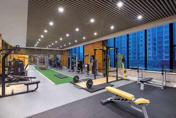 A gym with various exercise equipment, a green turf area, and large windows with a city view. - Wyndham Xinyang Downtown (Xinyang)