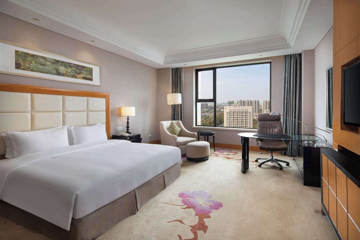 A hotel room with a large bed, a desk, a chair, and a TV.