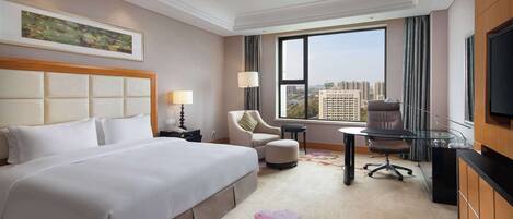 A hotel room with a large bed, a desk, a chair, and a TV.