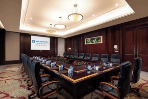 Un salón de conferencias con una larga mesa, varias sillas, una pantalla de proyector y un cuadro en la pared.